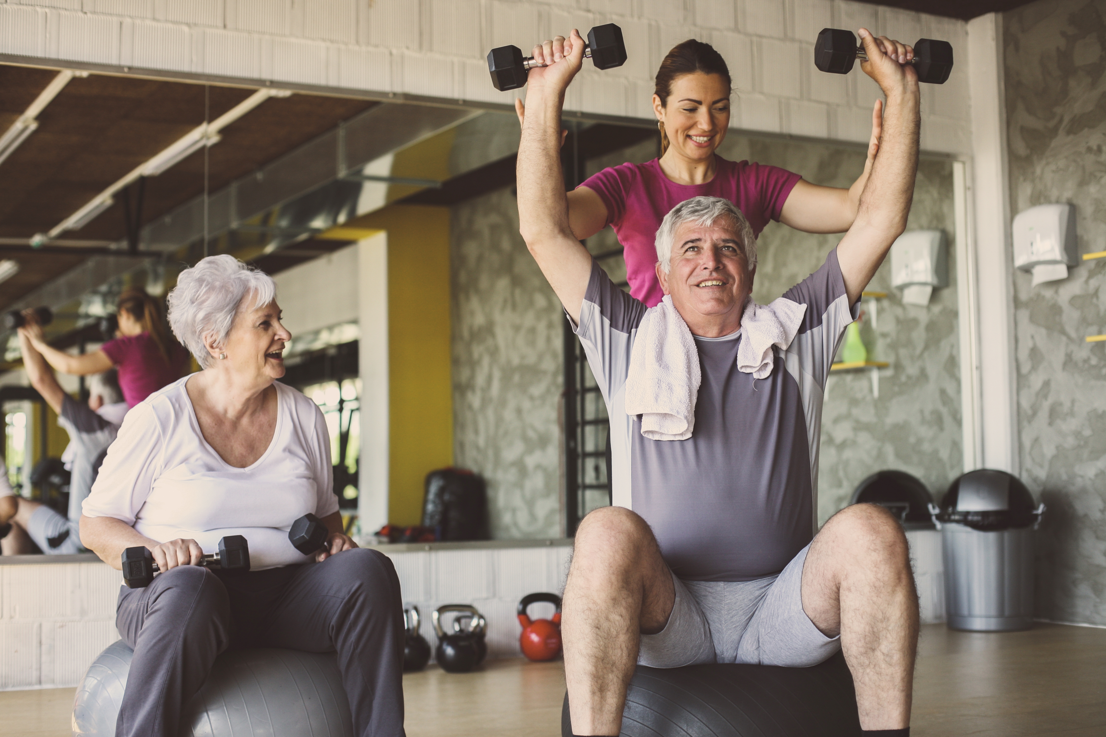 older man and woman in a gym working out with a personal trainer.